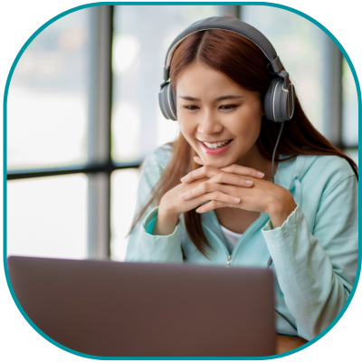 A lady working on a laptop wearing headphones, whilst smiling.