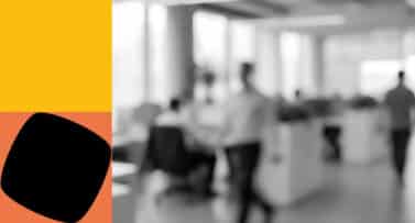 A blurred image of a person in a whit shirt walking past some desks in an office