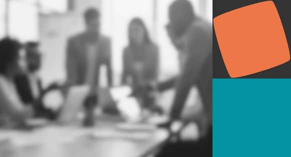 A blurred black and white image of people discussing over laptops with orange and teal shapes on the right hand side
