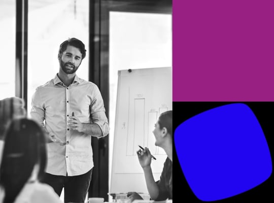 Black-and-white photo of a professional presenting to colleagues during a workshop or training session, alongside Agile Business Consortium certification branding in bold purple and blue graphic elements. The image conveys collaboration, learning, and professional development associated with Agile Business Consortium certifications