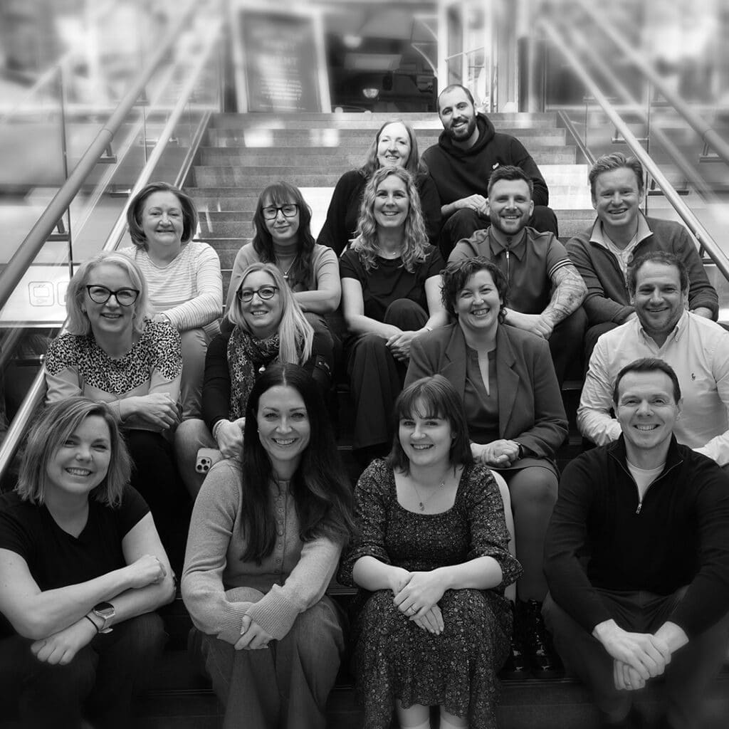 Black-and-white group photo of Agile Business Consortium team members smiling and sitting together on stairs