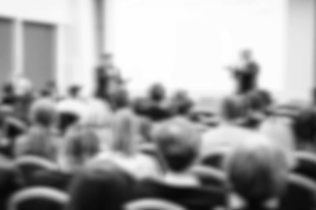 Blurred black-and-white conference audience and speakers, representing Agile Business Consortium events