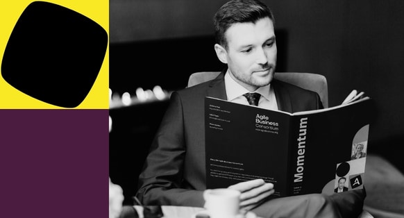 A black-and-white photograph of a suited man reading the Momentum Magazine Issue 4, alongside bold yellow, black, and deep-purple geometric blocks